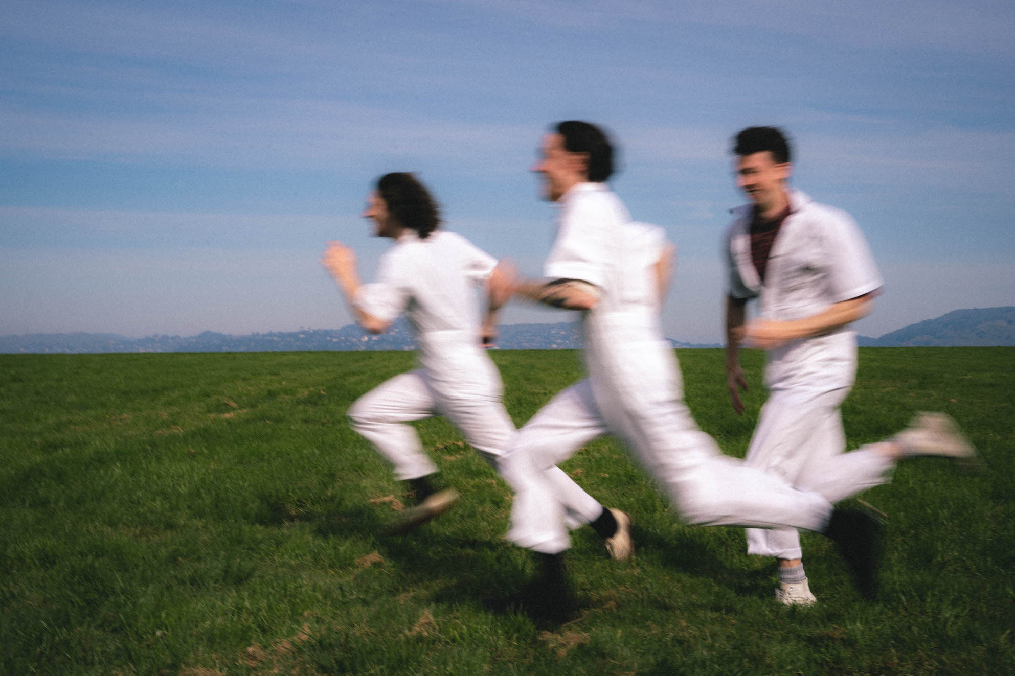 3 fellas in white jumpsuits run across the screen at lightning speed, floating above a bed of grass